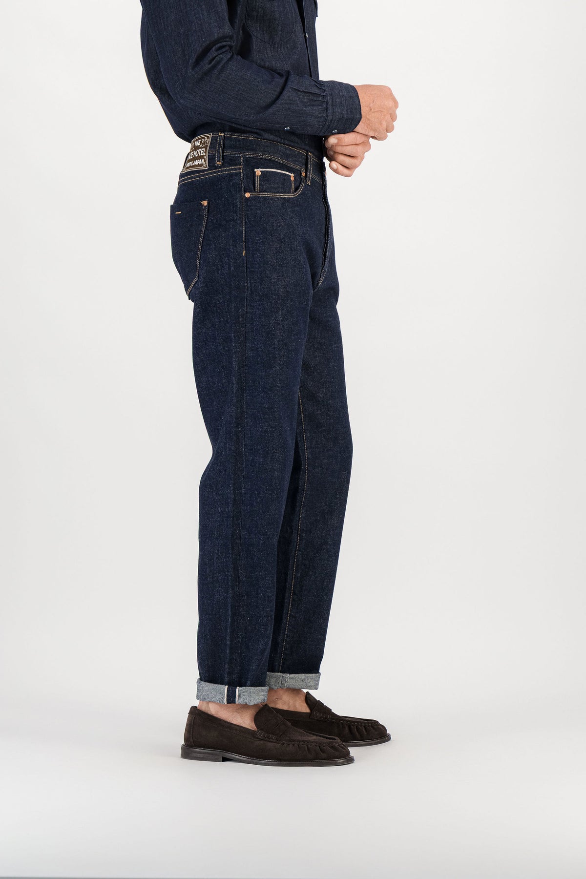 Raw indigo selvedge straight jeans side view, signature embroidered patch visible on waistband — AD 53 Selvedge Ace Denim Paris