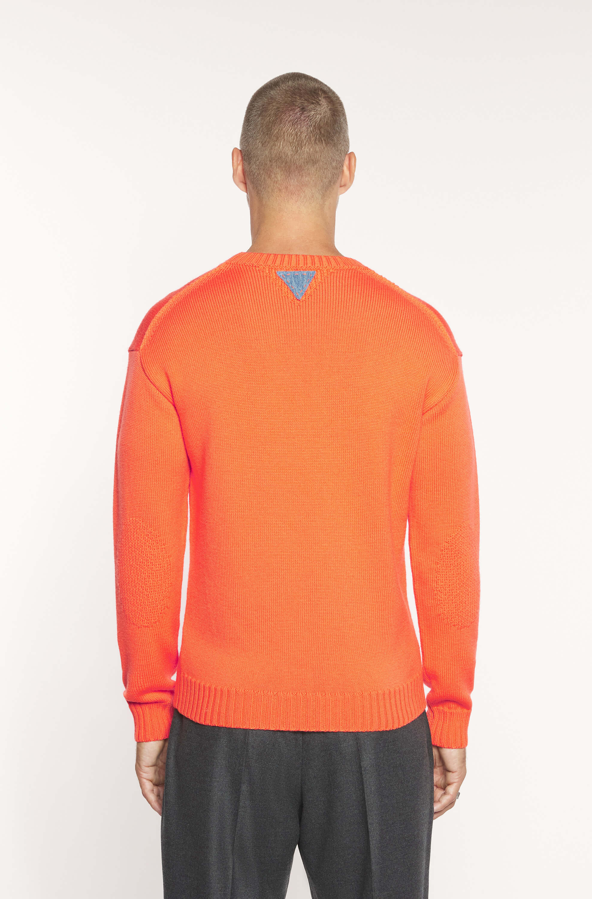 Rear view of the model wearing the orange round-neck sweater made of merino wool